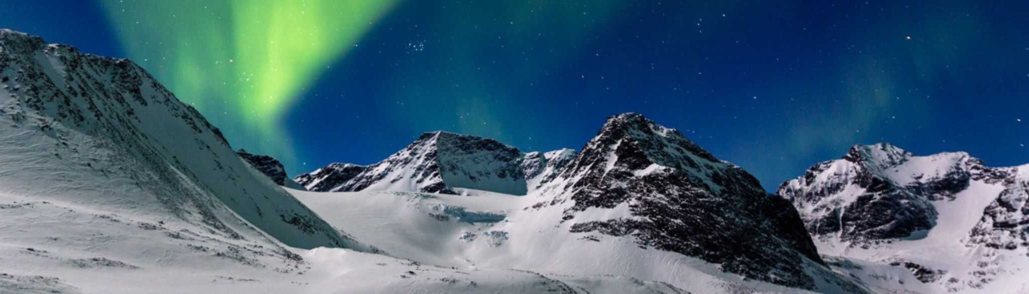 Met sneeuw bedekte bergen, waaronder de Kebnekaise, de hoogste berg van Zweden, liggen onder een helder, groen noorderlicht met een heldere sterrenhemel.