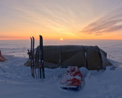 Schotel onder een polarzon met hoogteverschil, skispullen klaar voor een avontuur in de sneeuw, bij zonsondergang in de Arctic.