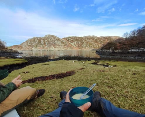 Rustige rivier in de natuur met twee mensen die genieten van een picknick op het gras.