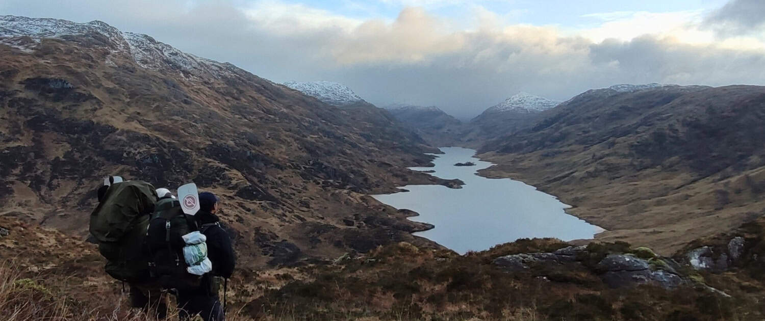 Wandelaar met rugzak in Schotse Highlands met meren en bergen, herfstkleuren, bewolkte hemel.
