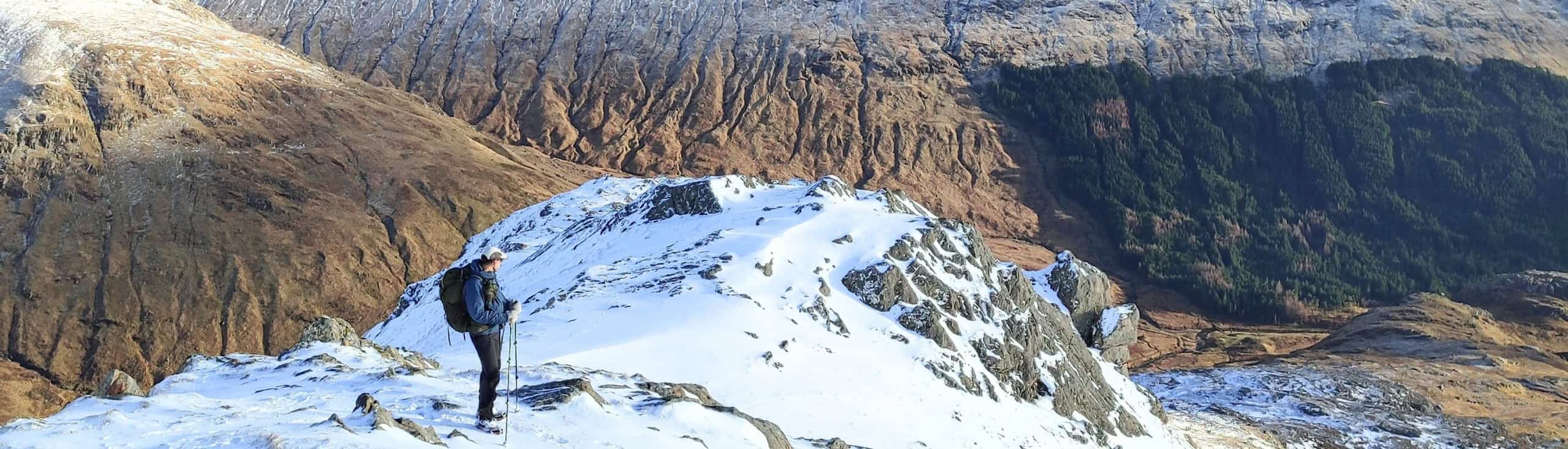 Eenzame wandelaar op besneeuwde bergtoppen met uitzicht op rots- en boslandschap in natuurgebied.