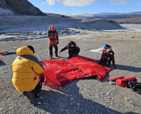 Team pitching a tent in a Greenland environment with ice and mountains in the background.