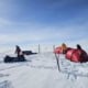 Snowmobile and tents in a snowy landscape under a blue sky.